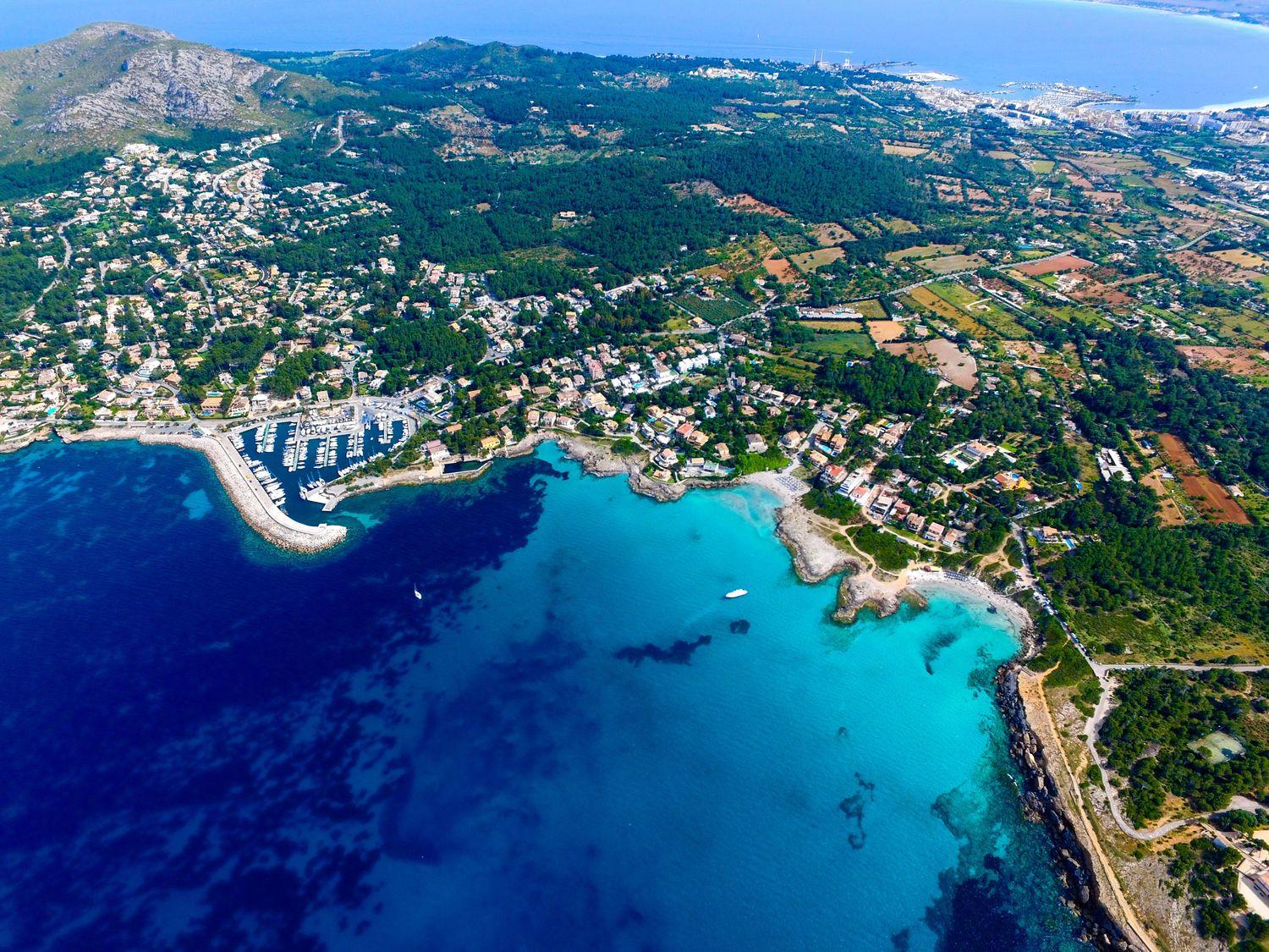 Blick von oben auf grünes Mallorca mit Hafenstädten, das blaue Meer und Yachten